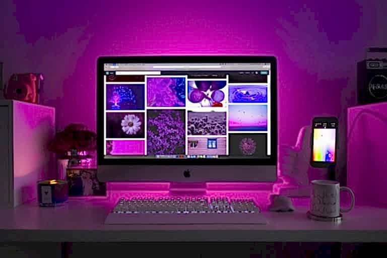 Modern desk setup with neon lighting and a desktop computer displaying colorful images. Bakı en iyi web tasarim ajansi