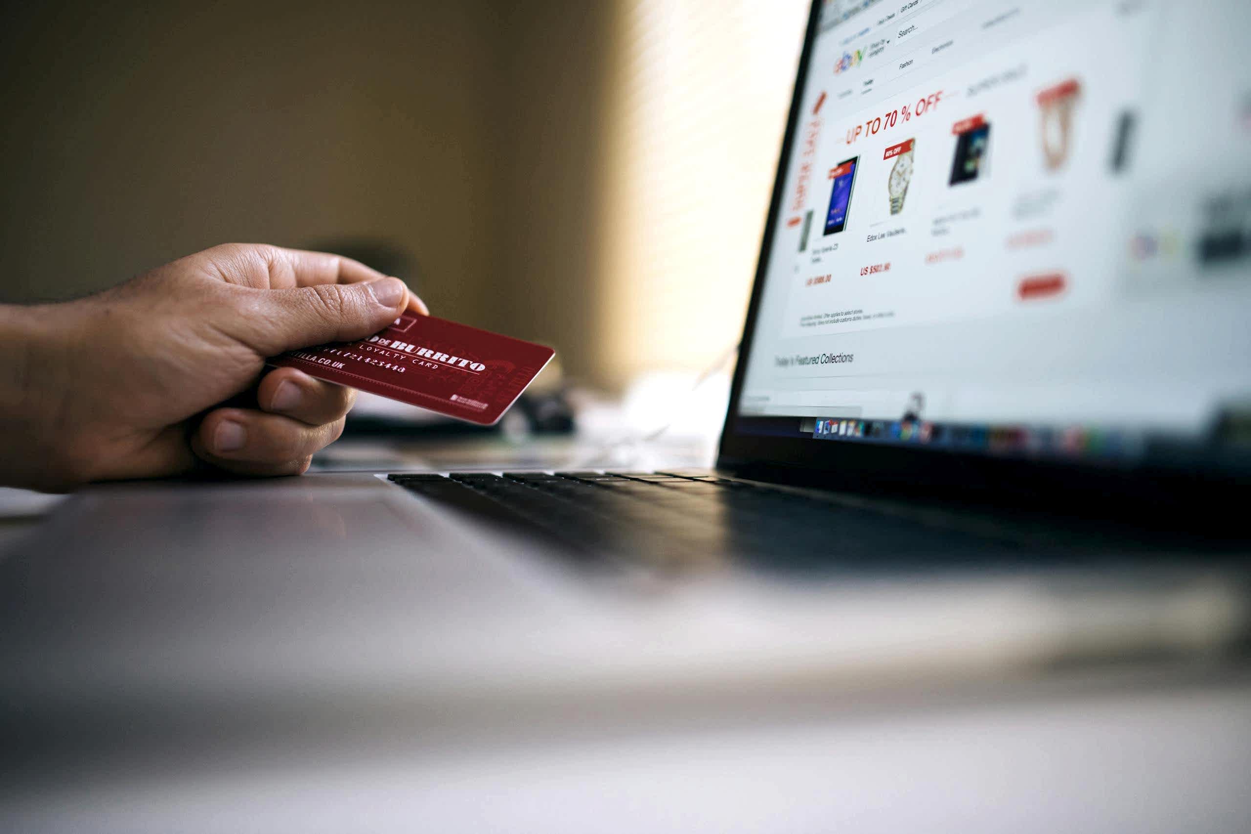 Person holding a credit card while shopping online on a laptop, indicating ecommerce transactions. Bakı e-ticaret web sitesi yapimi ve paketleri